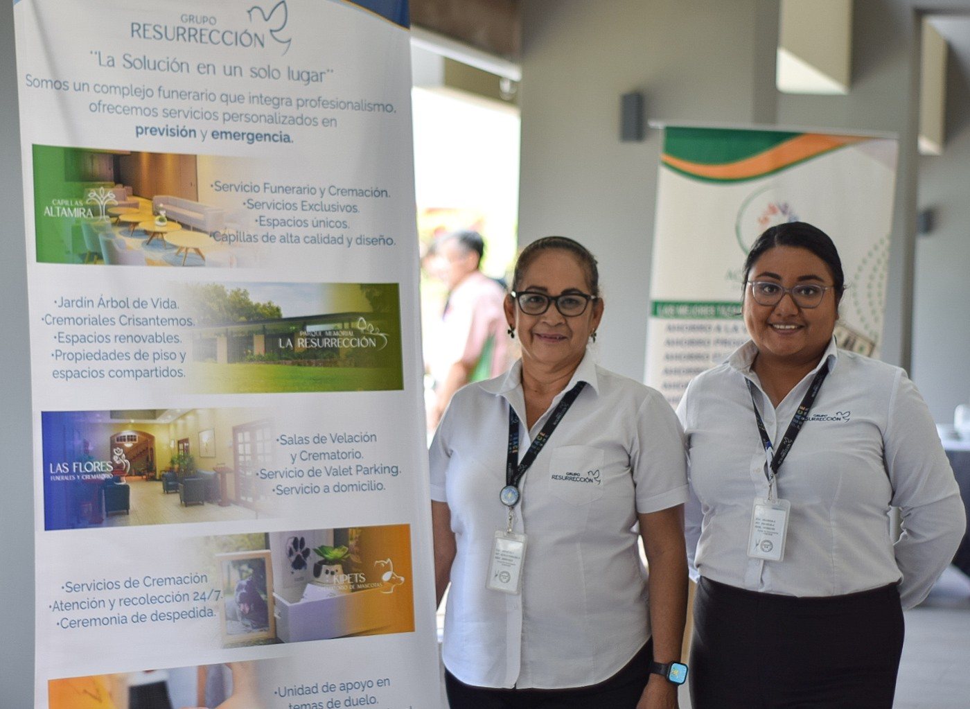 Dos colaboradoras junto a un banner promocional en un evento
